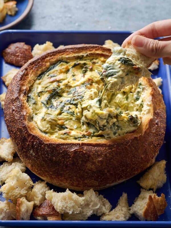 Woman dipping bread into spinach artichoke dip in a bread bowl.