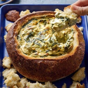 Woman dipping bread into spinach artichoke dip in a bread bowl.