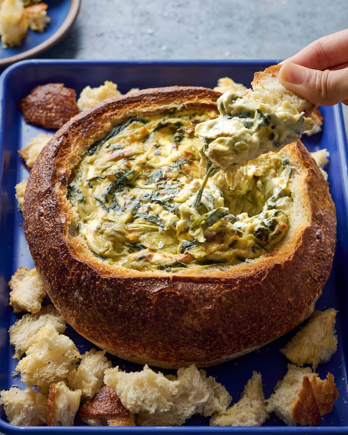 Woman dipping bread into spinach artichoke dip in a bread bowl.