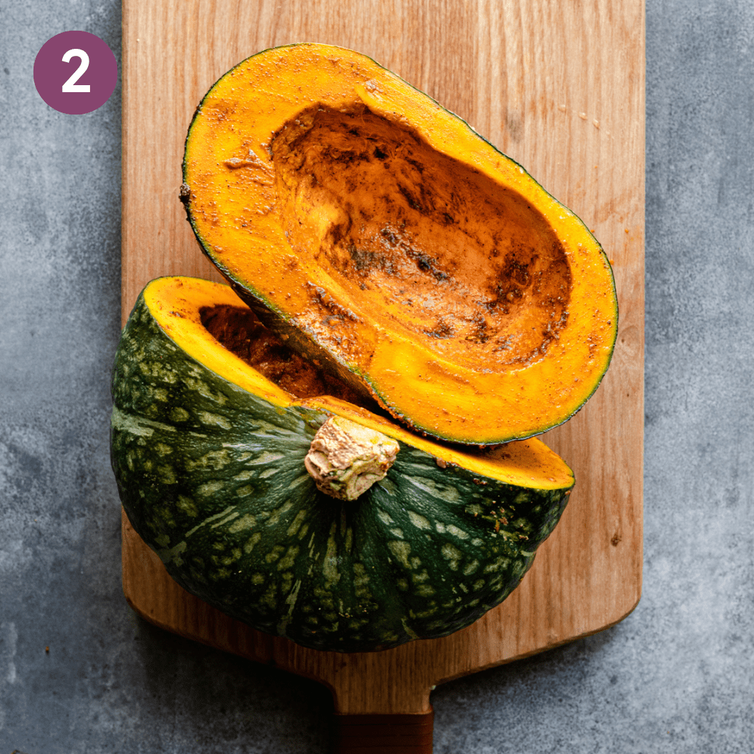 kabocha squash cut in half with spices rubbed in the flesh on a wooden cutting board.