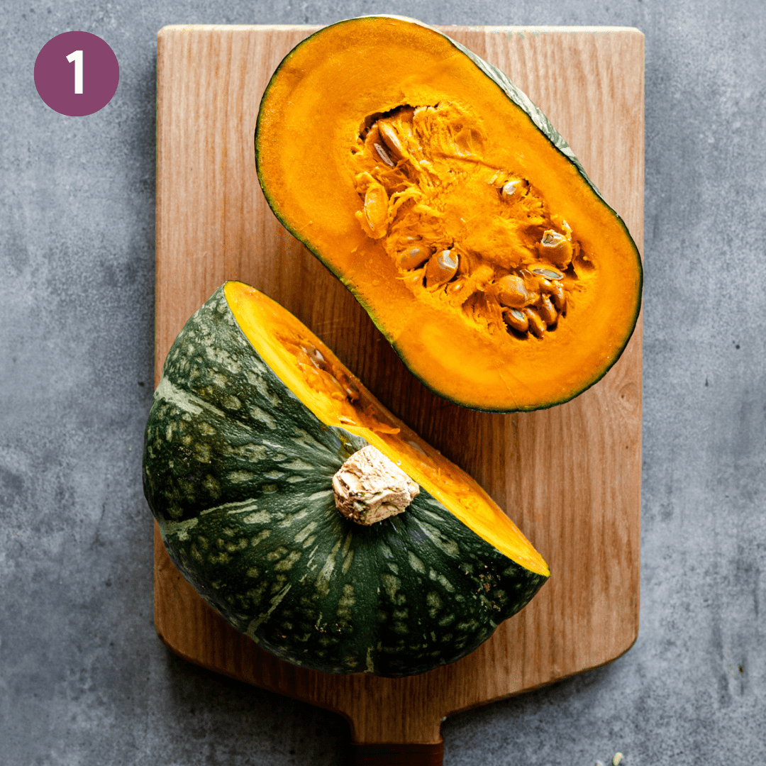 kabocha squash cut in ha on a wooden cutting board on a gray table.