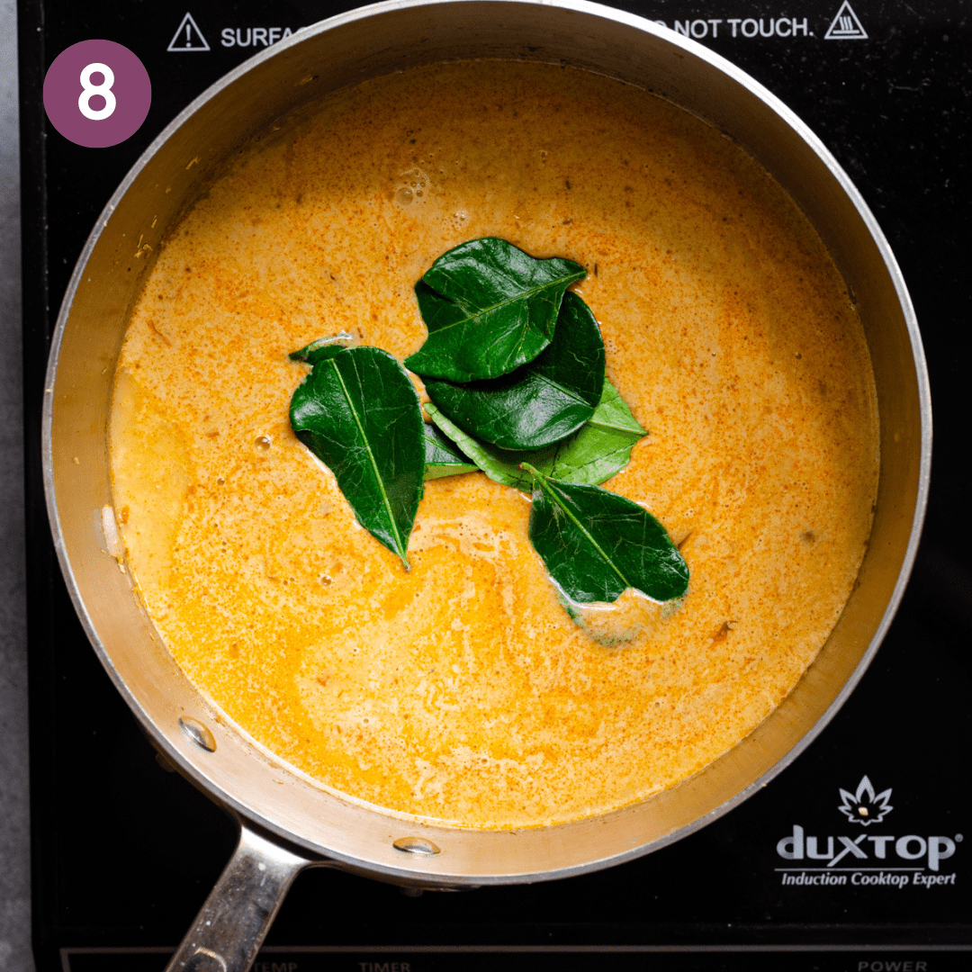 a beautiful golden coconut milk soup cooking in a stainless steel saucepan with whole lime leaves in the soup.