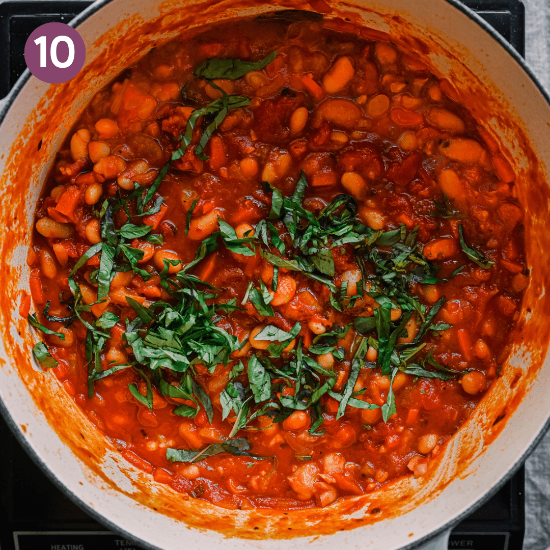 slivered basil garnished on top of thick and rich tuscan stewed beans with tomatoes in a dutch oven.