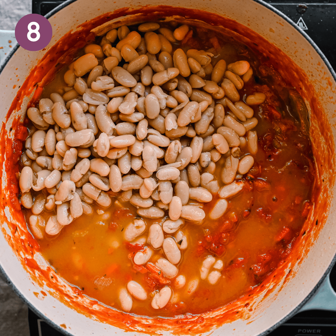 cannellini beans sitting on top of an italian tomato stew with vegetable broth in a dutch oven. 