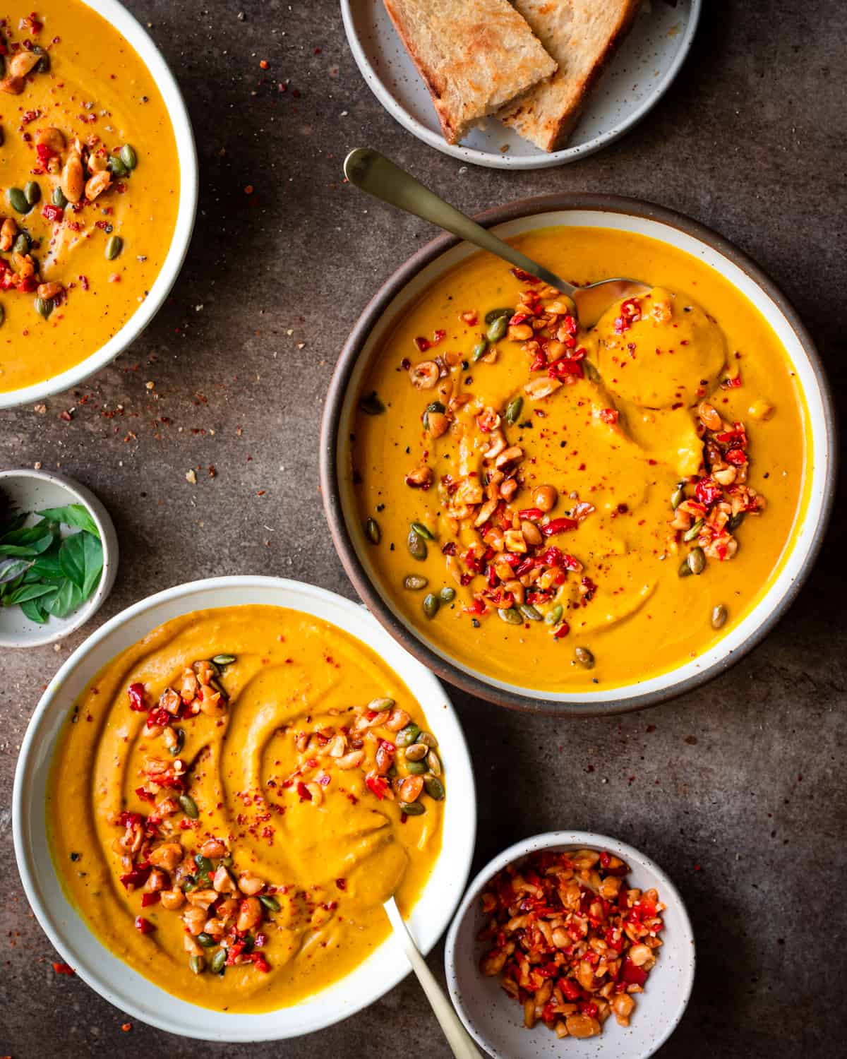 three bowls of thai pumpkin soup garnished with chili peppers on a brown table.