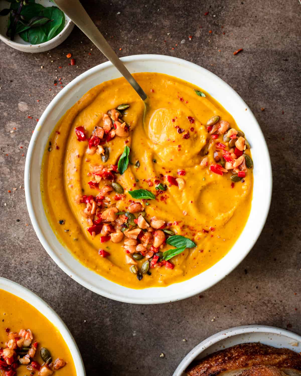 a bowl of thai pumpkin soup with a spoon showing its creamy texture, garnished with thai basil and chili peppers.