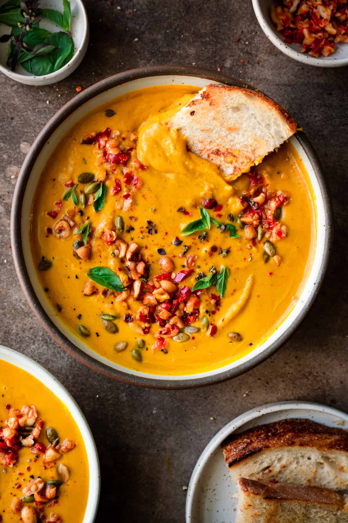 a bowl of thai pumpkin soup with a piece of toasted bread dunking in to show its creamy texture.