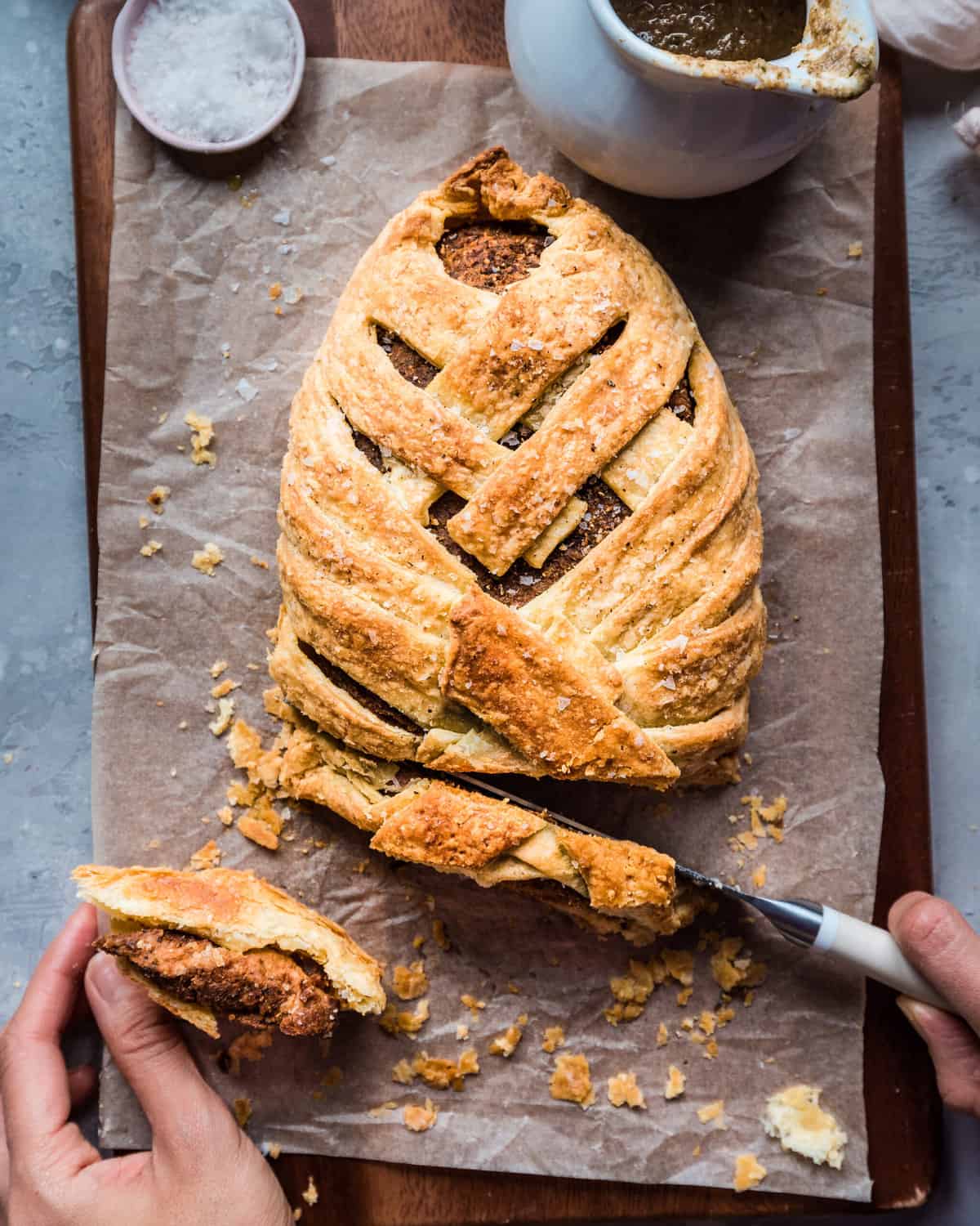 woman's hands slicing a vegan mushroom wellington on a parchment paper lined cutting board.