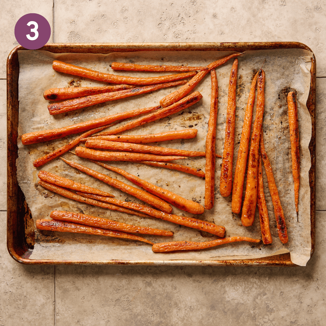 roasted carrots on a parchment paper lined sheet pan on a beige tiled surface. 