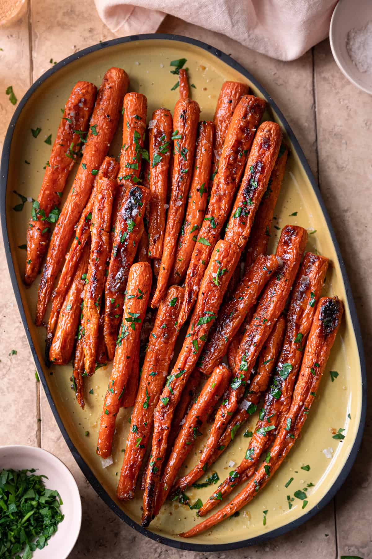 maple roasted carrots garnished with parsley on a yellow serving tray on a light pink tiled surface.