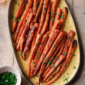 maple roasted carrots on a yellow serving tray, garnished with parsley, on a tiled surface.