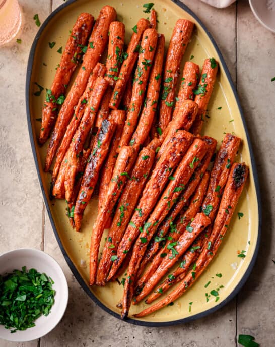 maple roasted carrots on a yellow serving tray, garnished with parsley, on a tiled surface.