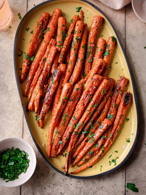 maple roasted carrots on a yellow serving tray, garnished with parsley, on a tiled surface.