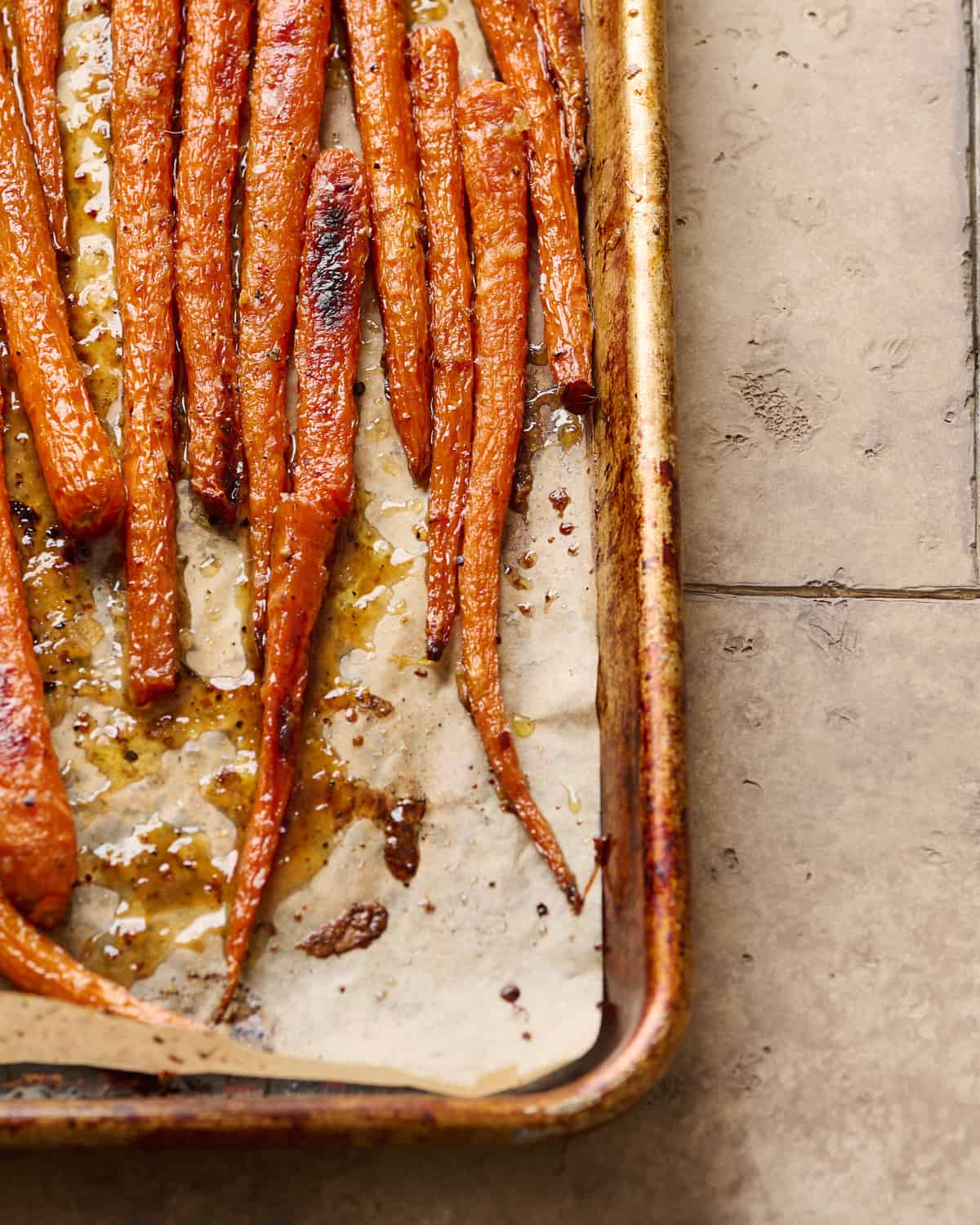 closeup angled shot of maple roasted carrots on a parchment paper lined sheet pan.