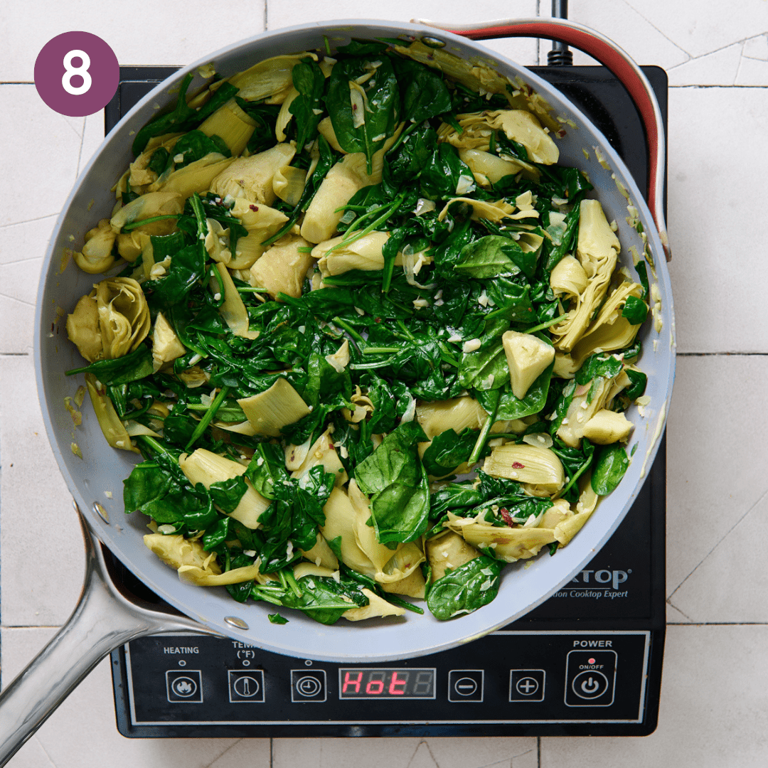 Spinach mixed with artichoke mixture in pan.