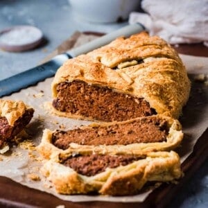 vegan mushroom wellington cut into slices on a parchment paper lined cutting board on a gray table.