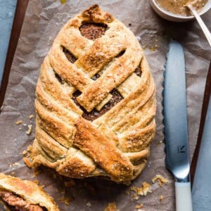 vegan mushroom wellington with one piece sliced open on a wooden cutting board with gravy.