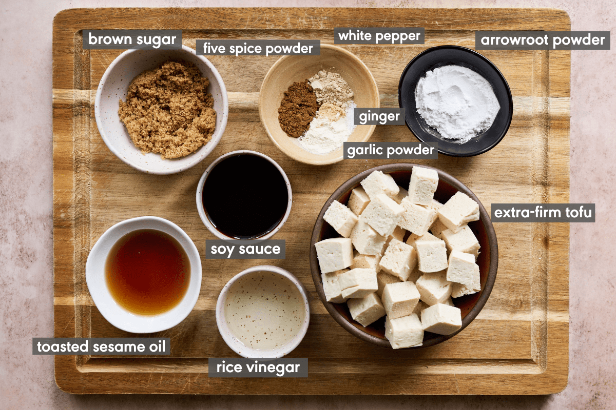 ingredients for vegan marinated tofu laid out on a wooden cutting board in bowls and labeled. 