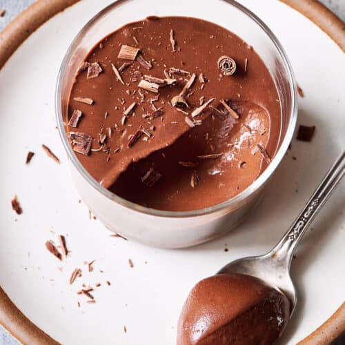 Chocolate mousse in a glass ramekin on a white plate on a table.