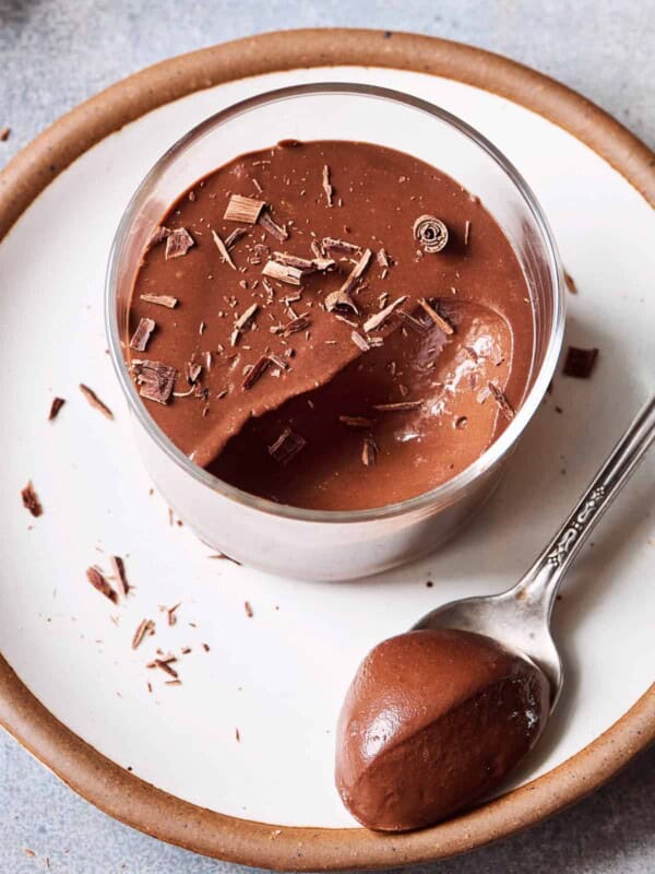 Chocolate mousse in a glass ramekin on a white plate on a table.