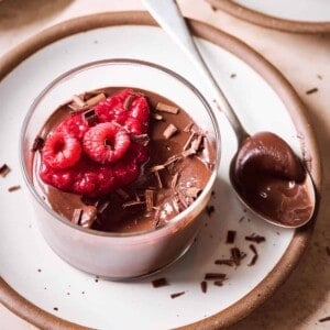 Chocolate mousse with raspberry compote and raspberries in glass ramekin on white plate.