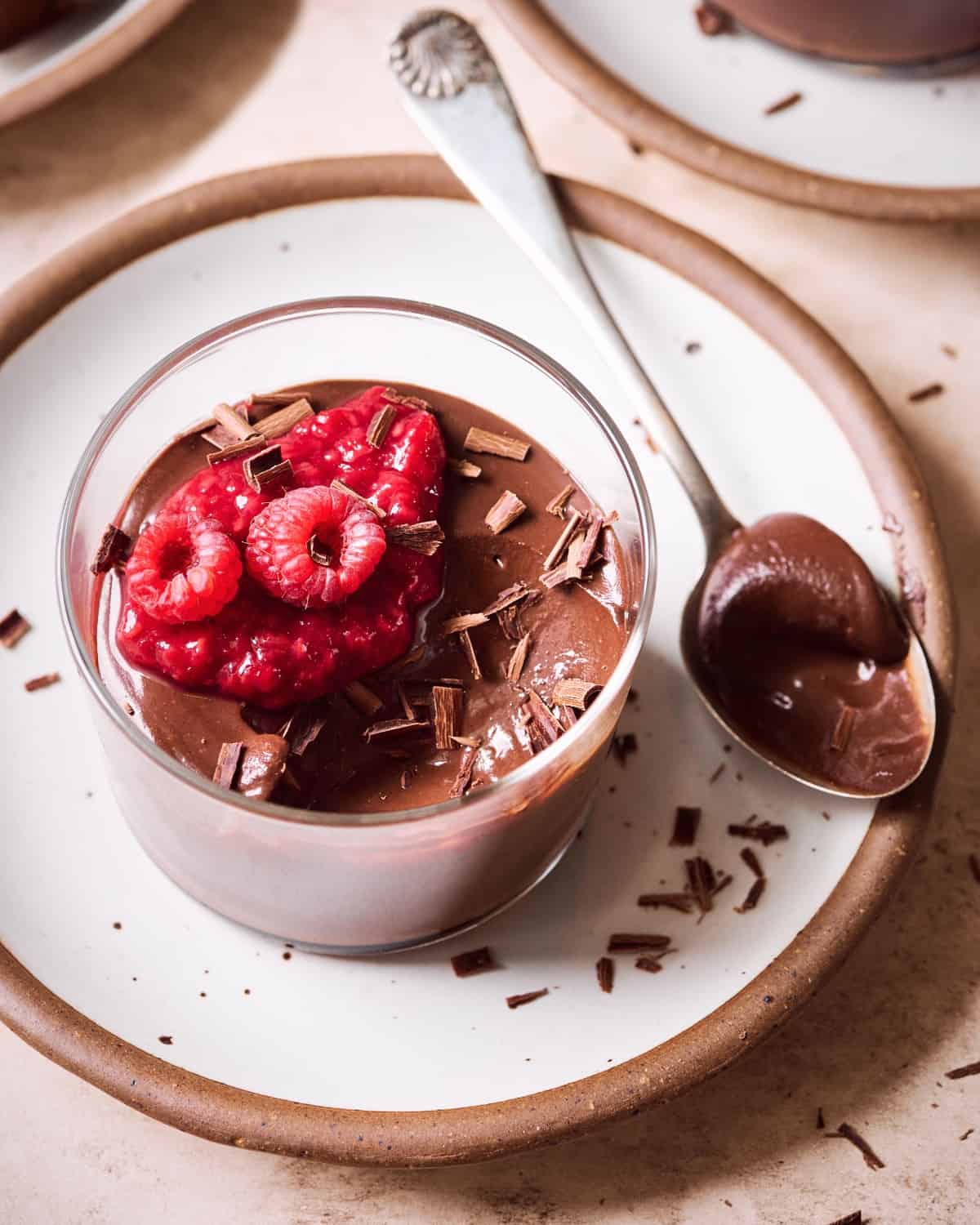 Chocolate mousse with raspberry compote and raspberries in glass ramekin on white plate.