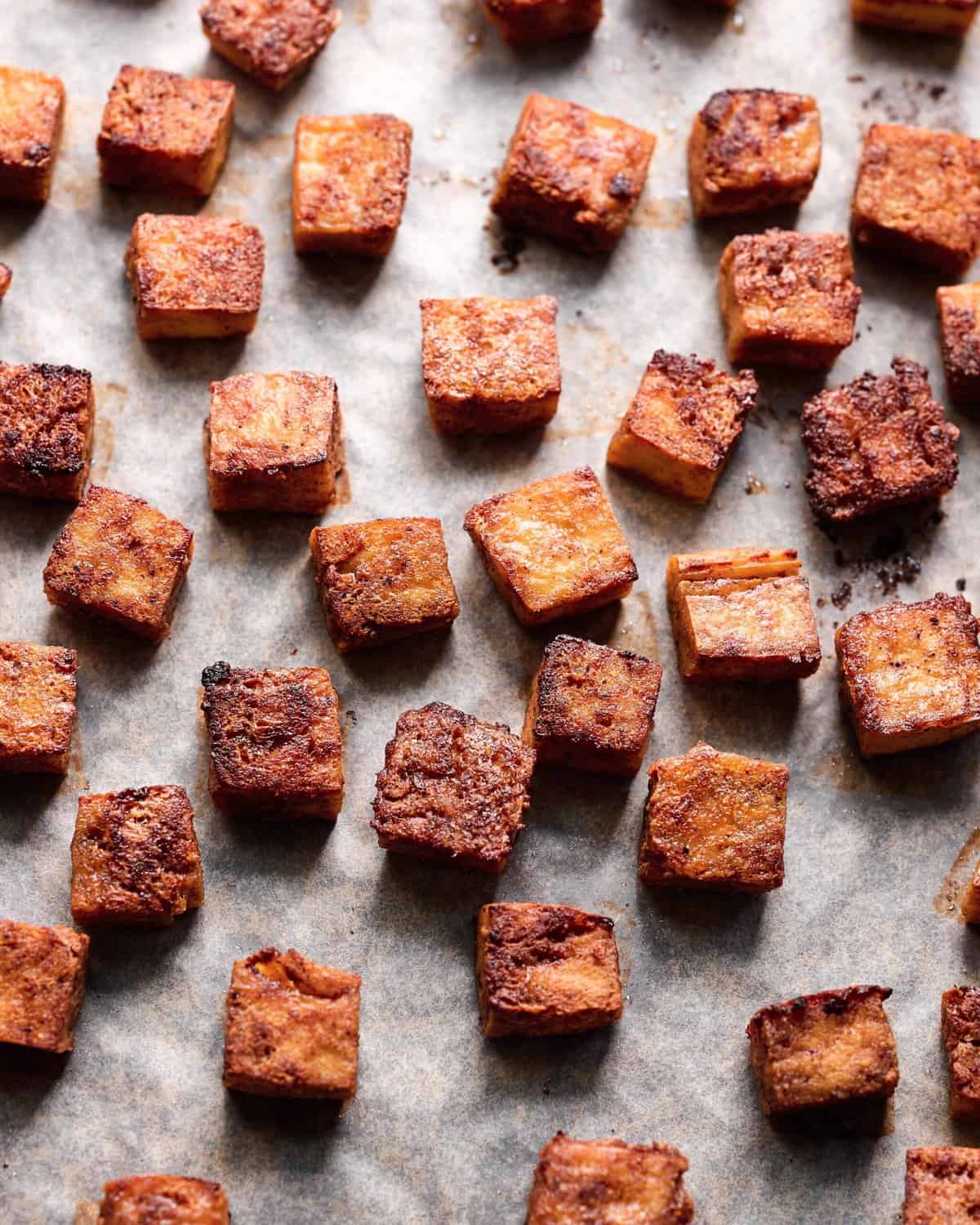 crispy browned marinated tofu cubes on a parchment paper lined sheet pan. 