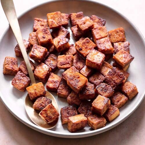 crispy browned marinated tofu cubes in a ceramic bowl with a spoon.