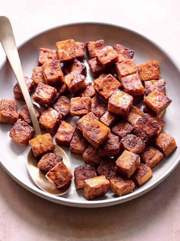 crispy browned marinated tofu cubes in a ceramic bowl with a spoon.