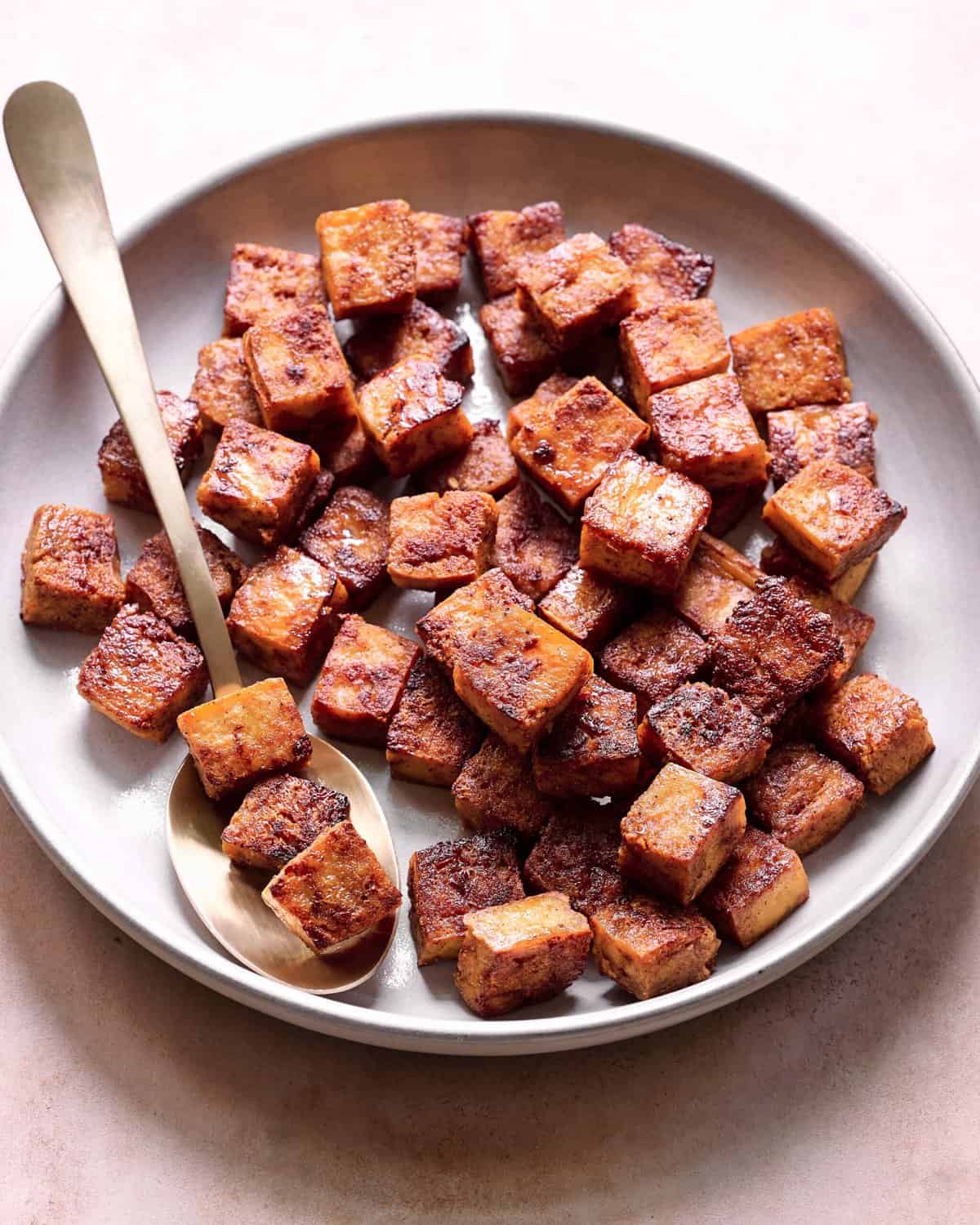 crispy browned marinated tofu cubes in a ceramic bowl with a spoon. 