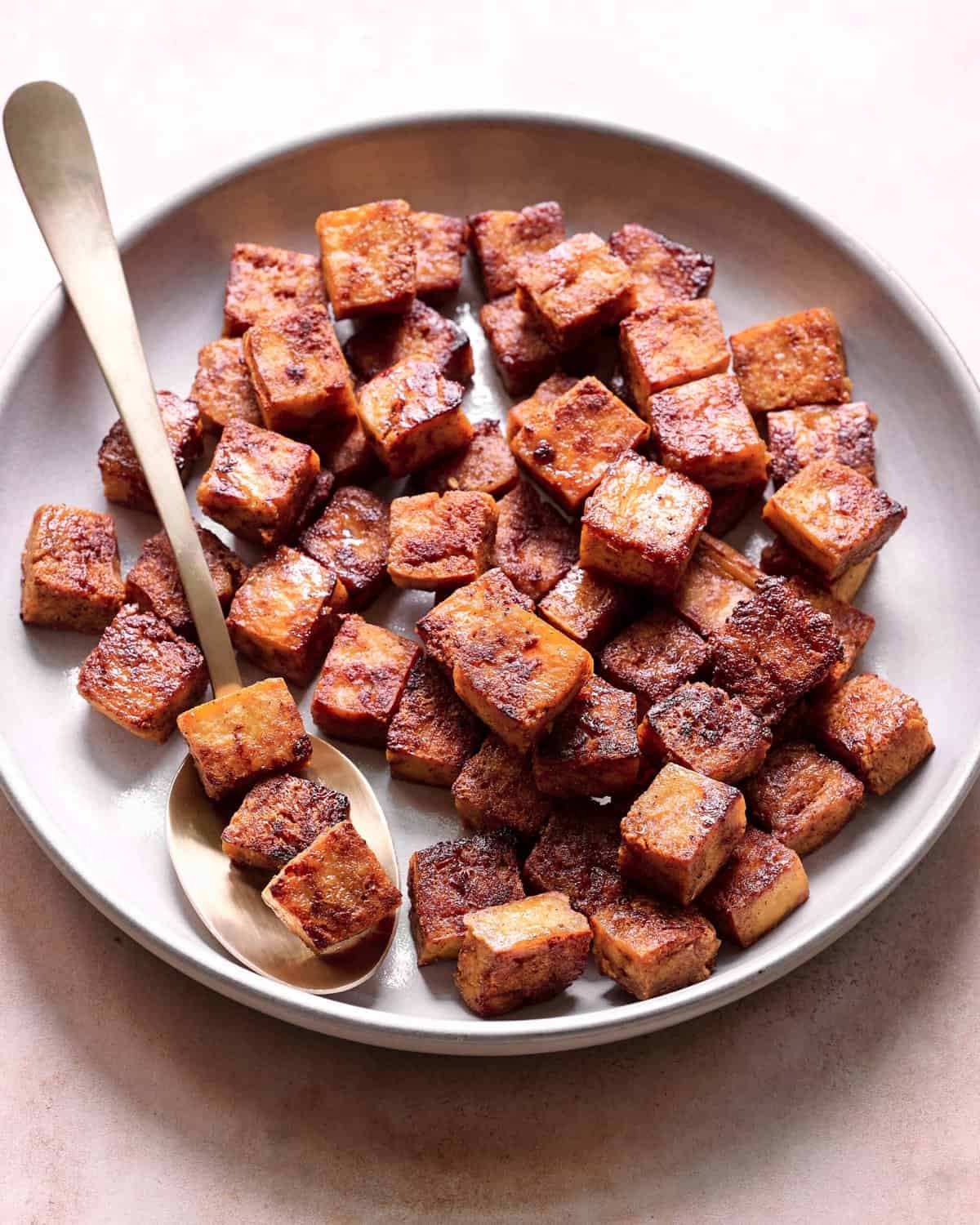 crispy browned marinated tofu cubes in a ceramic bowl with a spoon.