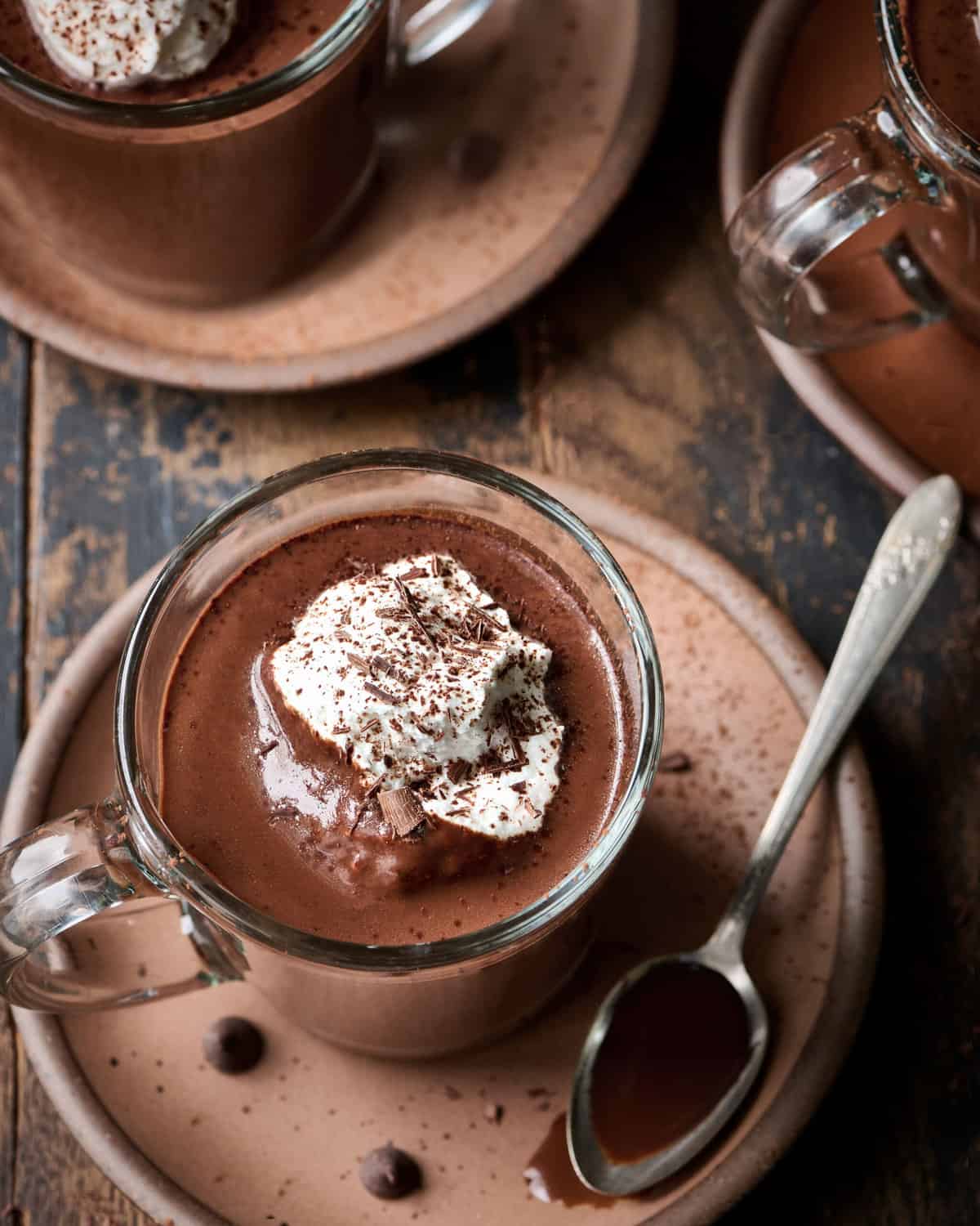 Overhead view of three mugs of hot chocolate with whipped cream on a plate on a wood table.