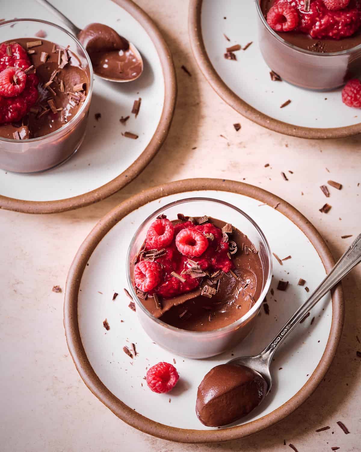 Three ramekins of chocolate mousse with raspberry compote and raspberries on a white plate.
