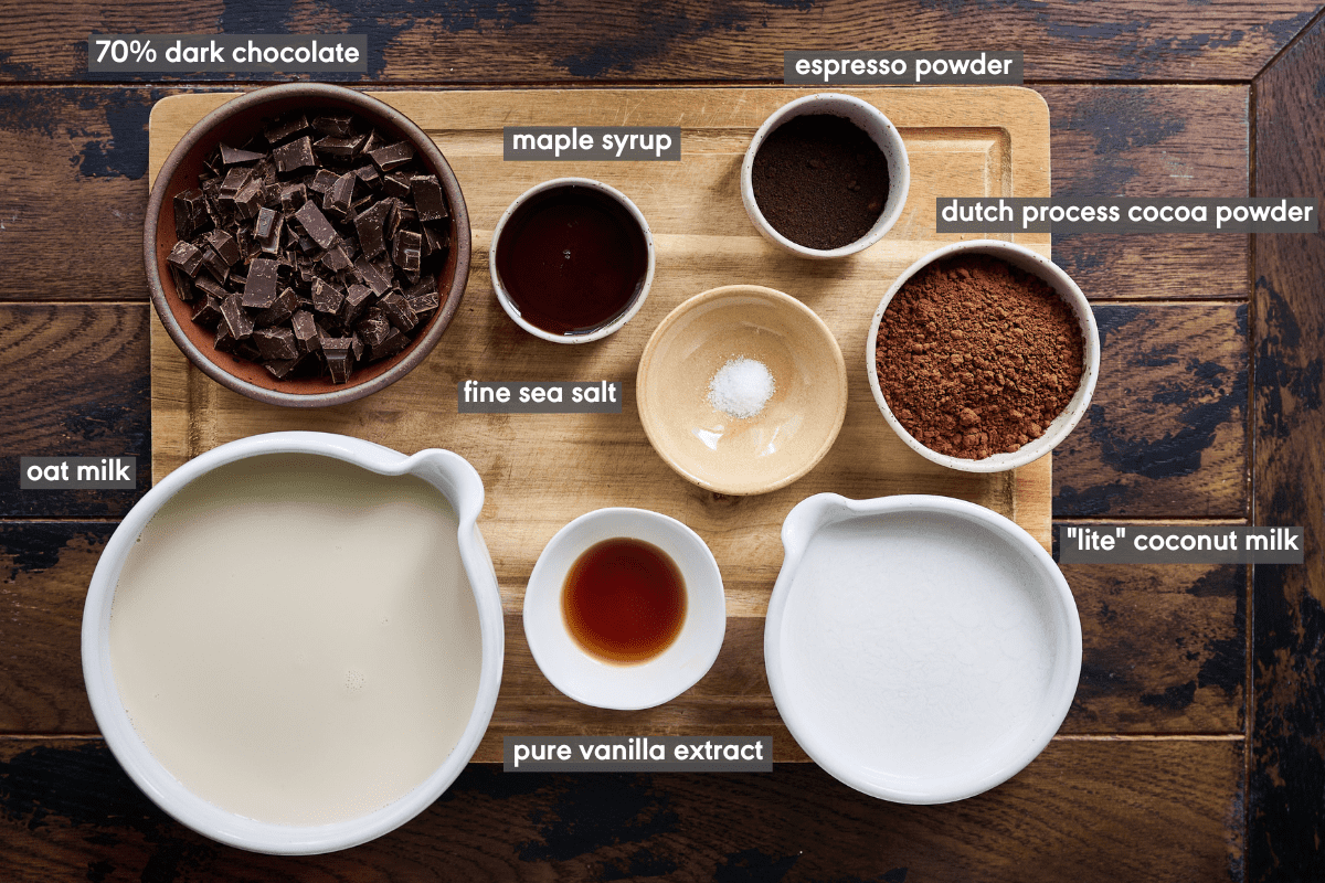 Hot chocolate ingredients in various bowls on a wood cutting board on a wood table.