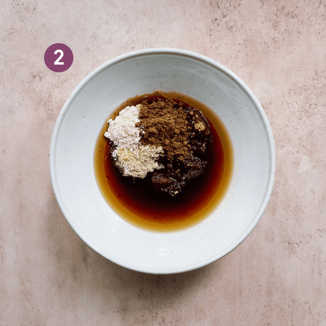 soy sauce and spices in a white ceramic bowl for a tofu marinade on a pink table.