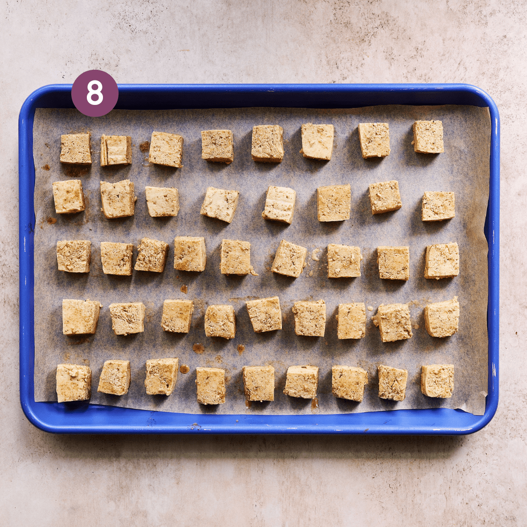 marinated tofu cubes arranged in a single layer on a parchment paper lined blue sheet pan.