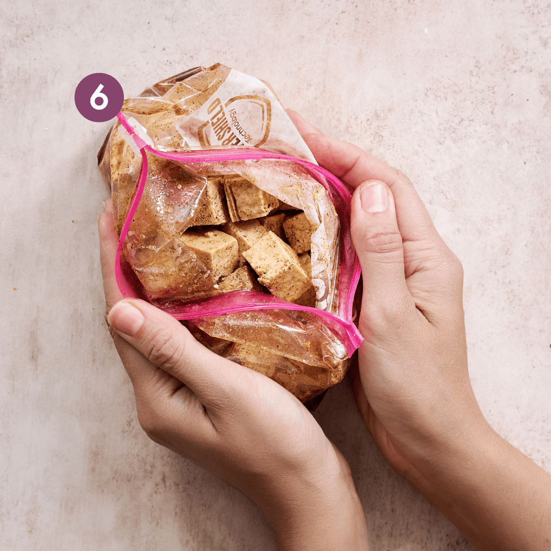 woman's hands cupping a ziploc bag with cubes of marinated tofu cubes..