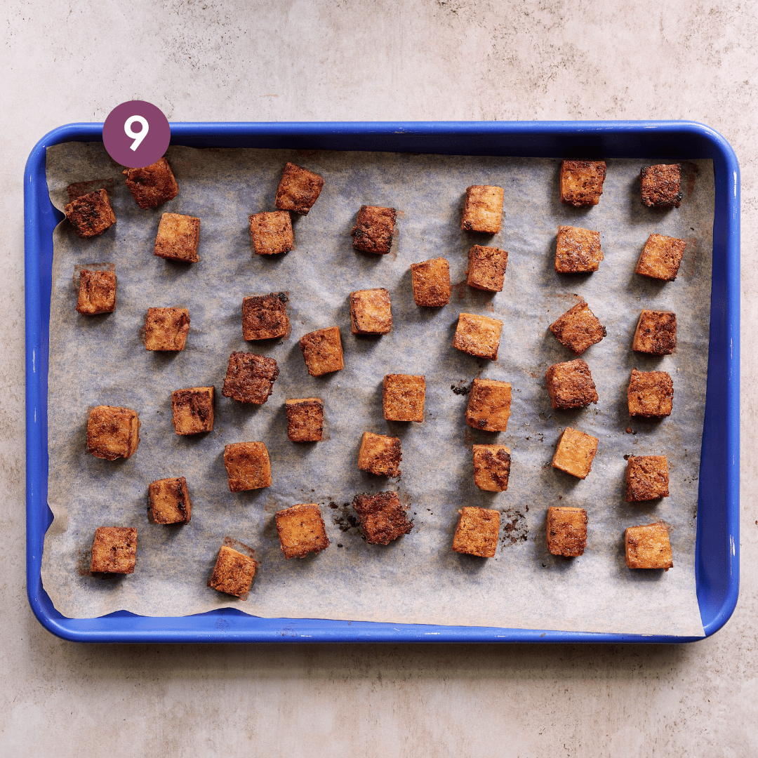 baked marinated tofu cubes looking browned and crispy on a parchment paper lined sheet pan.