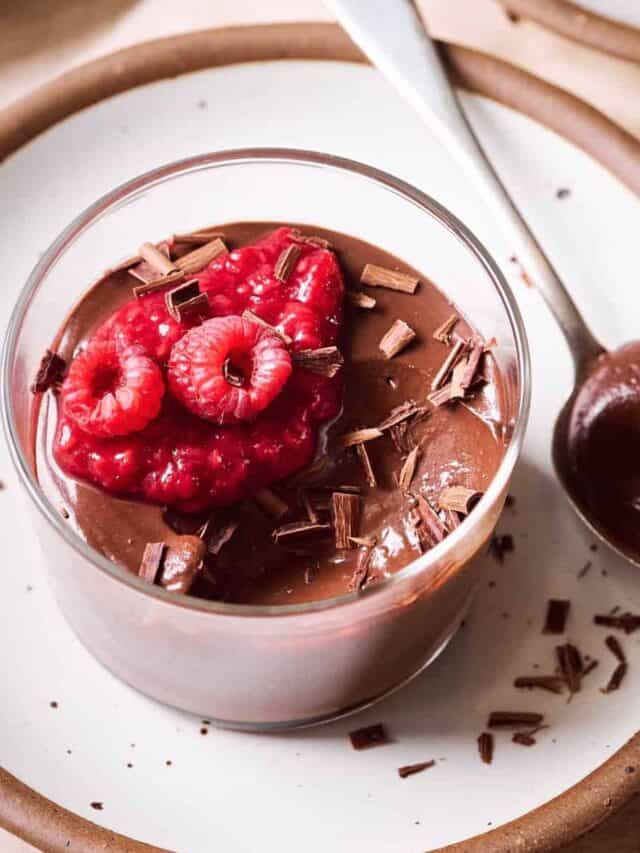 Chocolate mousse with raspberry compote and raspberries in glass ramekin on white plate.