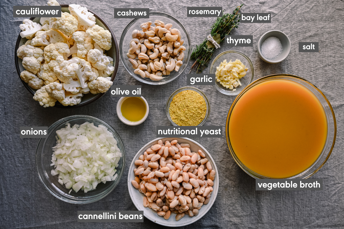 ingredients for vegan cauliflower soup in bowls on a tablecloth with each ingredient labeled.