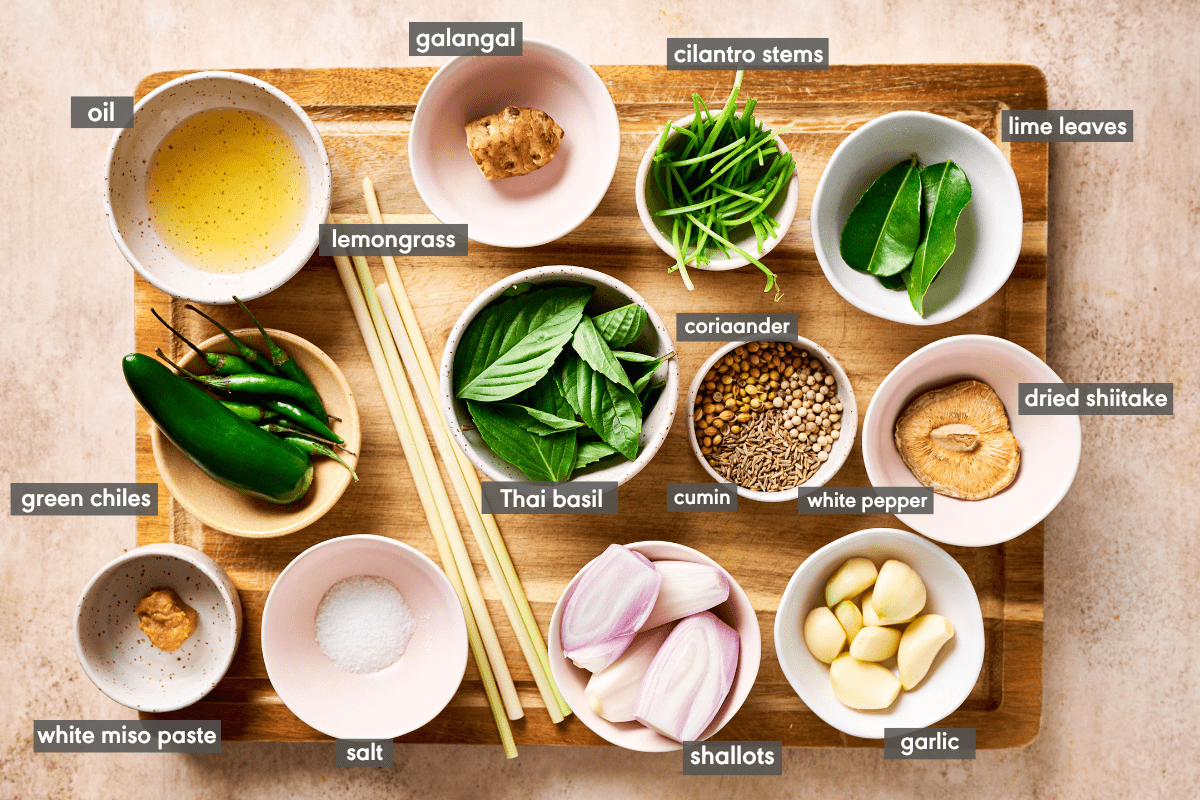 ingredients for authentic Thai green curry paste on a wooden cutting board with ingredients labeled.