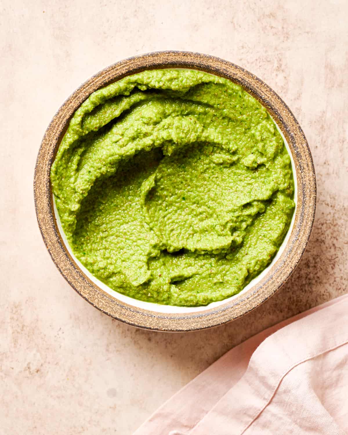 white ceramic bowl filled with vibrant green homemade thai curry paste on a light pink surface. 