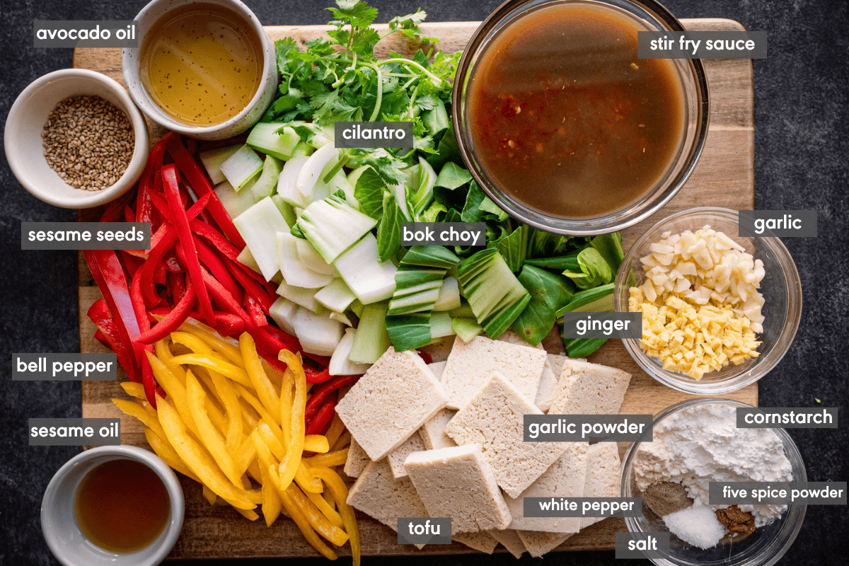 Tofu stir fry ingredients chopped and in various bowls on a wooden cutting board.