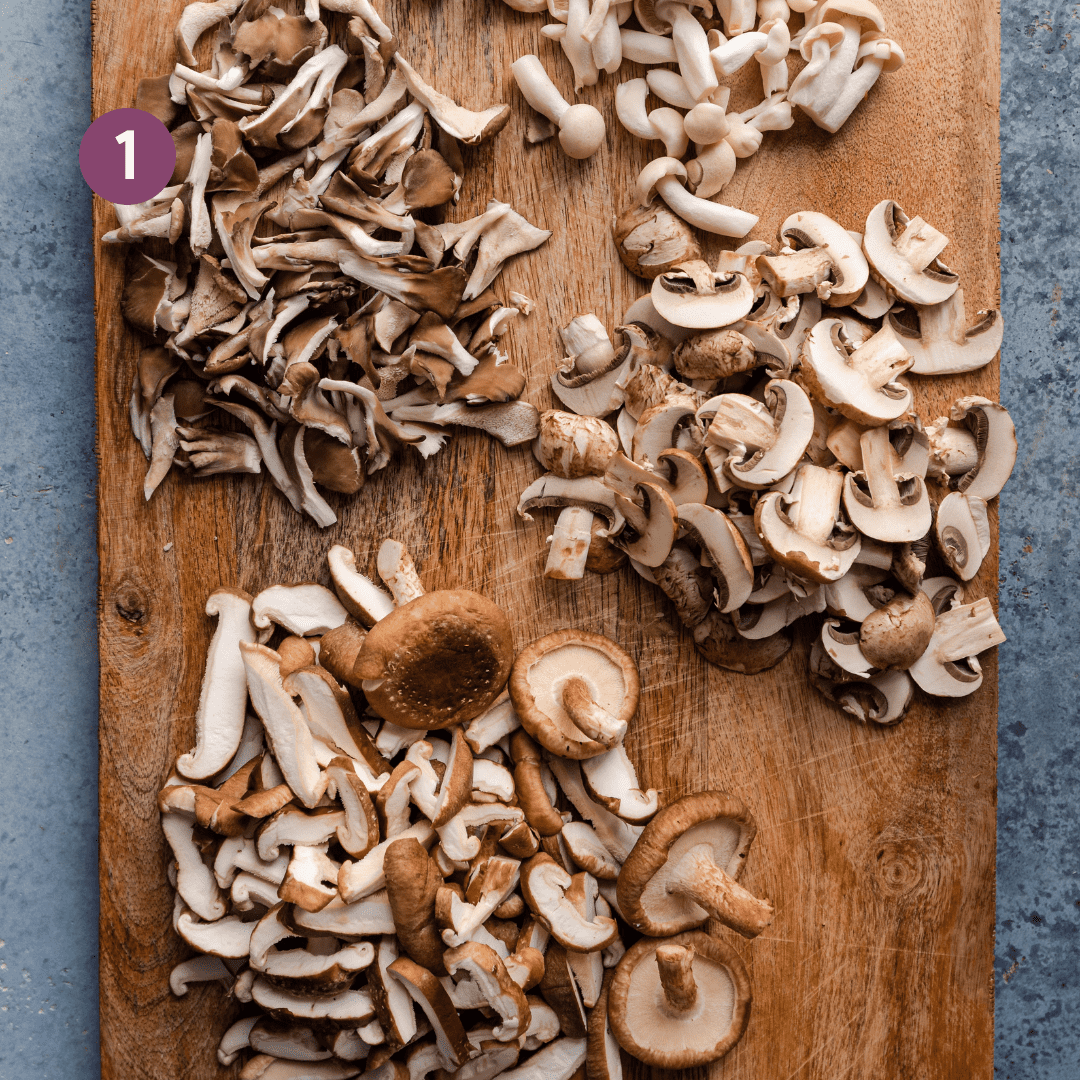 different varieties of mushrooms sliced or torn on a wooden cutting board. 