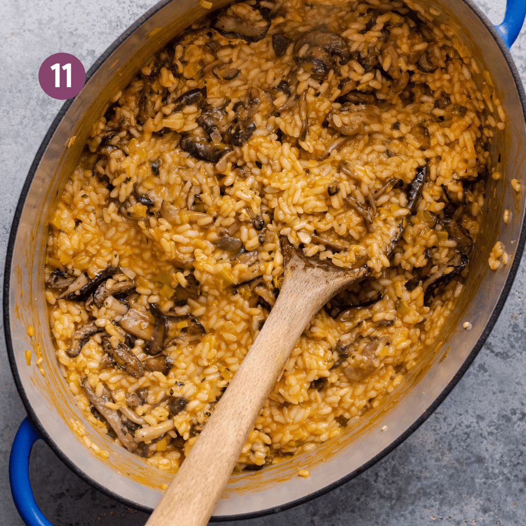 vegan risotto with mushrooms in a large dutch oven with a wooden spoon dug into the risotto. 