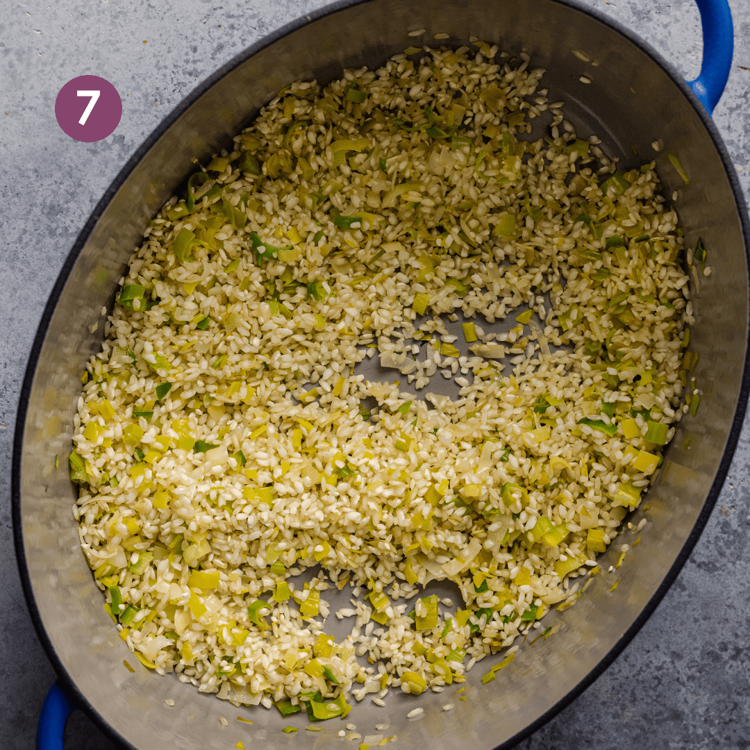 arborio rice being toasted with leeks and garlic in a large dutch oven for risotto.