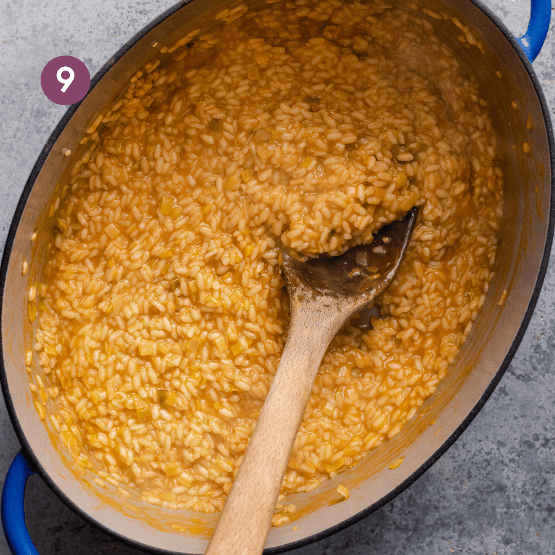 creamy golden vegan risotto in a large dutch oven with a wooden spoon dug into the risotto to show texture. 