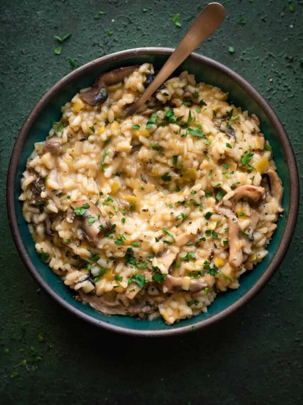 creamy, velvety vegan mushroom risotto in a green bowl with spoon dug in on a dark green table.