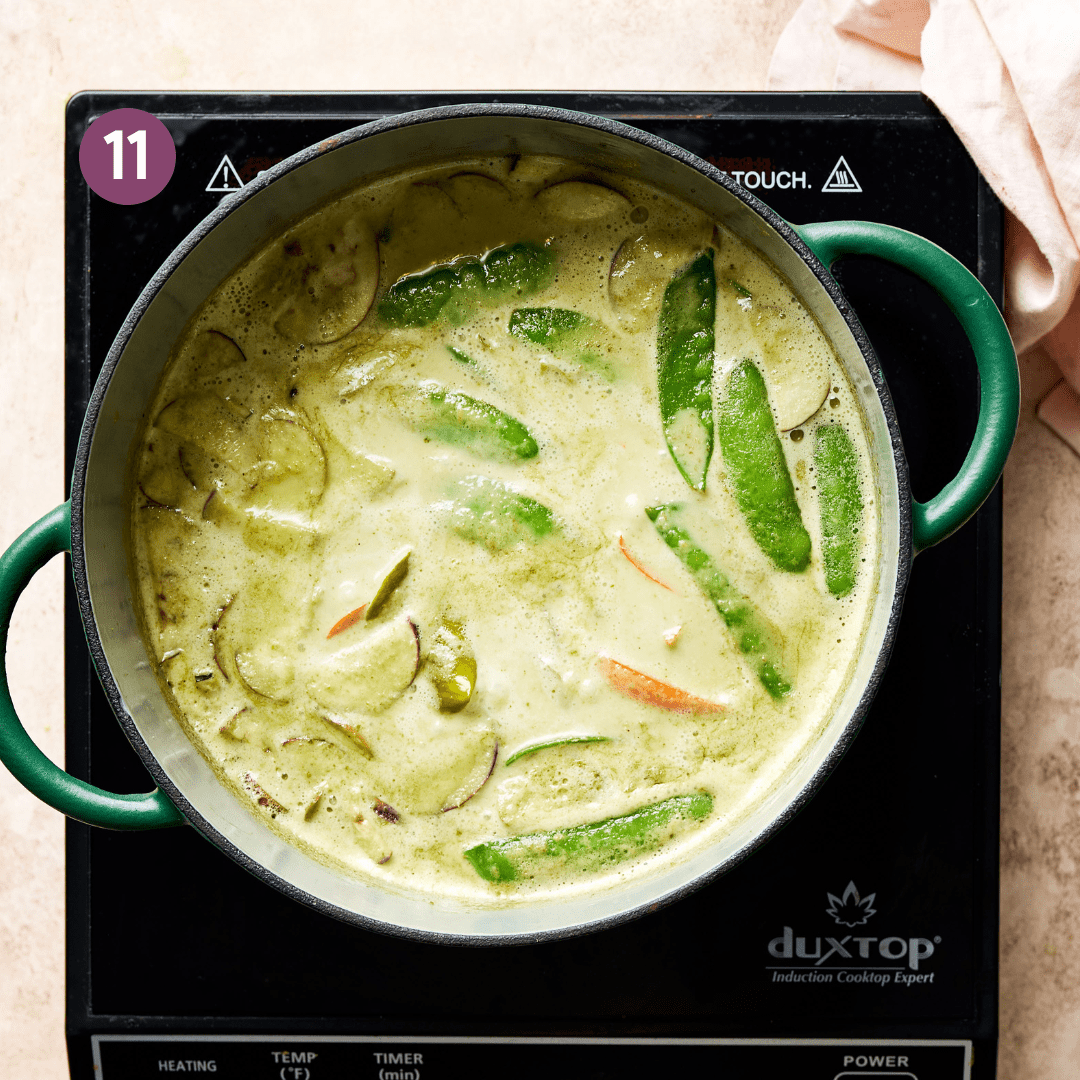 vegetables simmering in a vegan thai green curry in a green saucepan. 