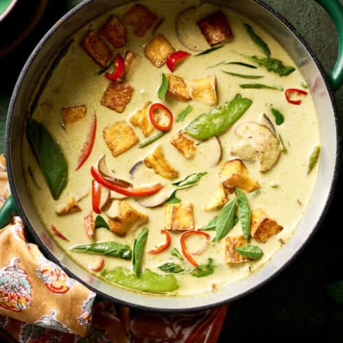 vegan thai green curry with vegetables and crispy tofu in a green saucepan on a green table.